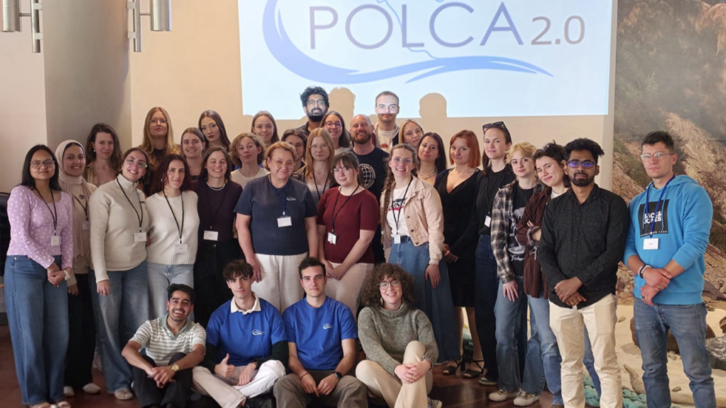 Fotografia grupowa uczestników na tle banneru POLCA 2.0
